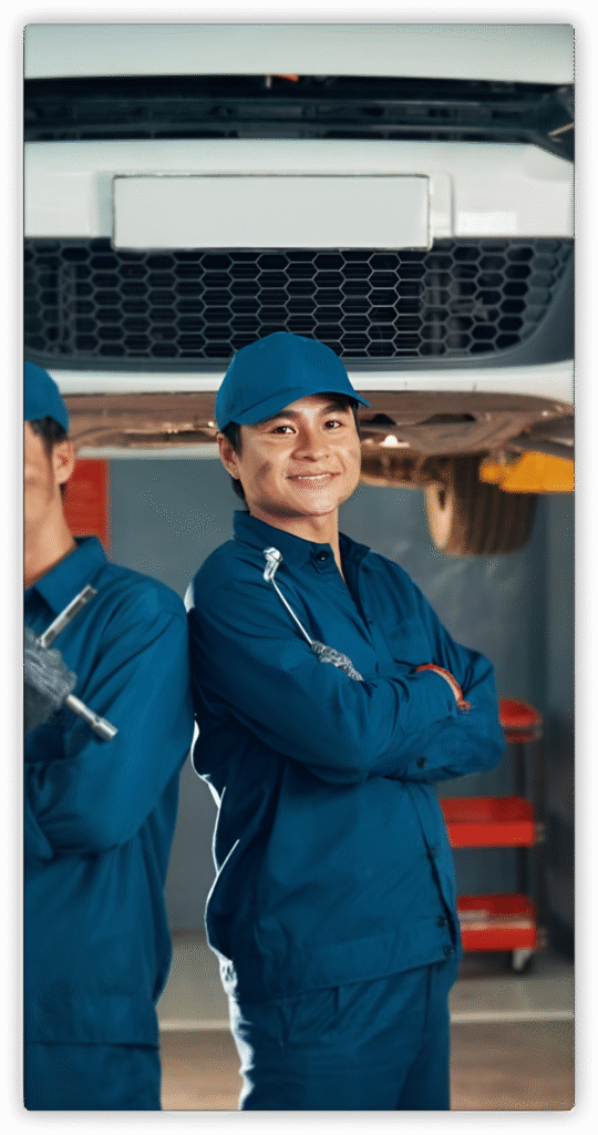 Experienced YBR auto mechanic proudly standing in the workshop under a lifted vehicle, ready to deliver expert car repair and maintenance services. Trust YBR for professional, reliable automotive care.